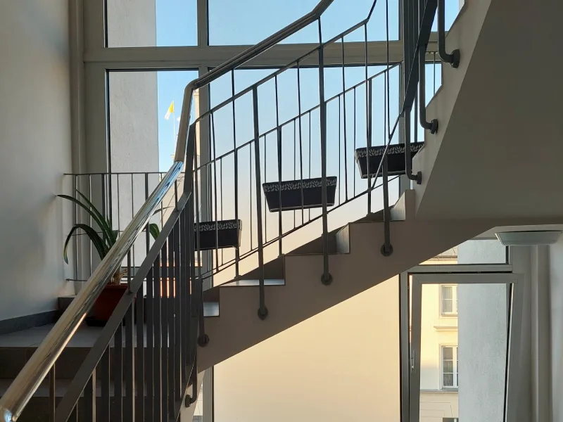 Modernistyczna klatka schodowa z geometrycznymi schodami i widokiem na okno.